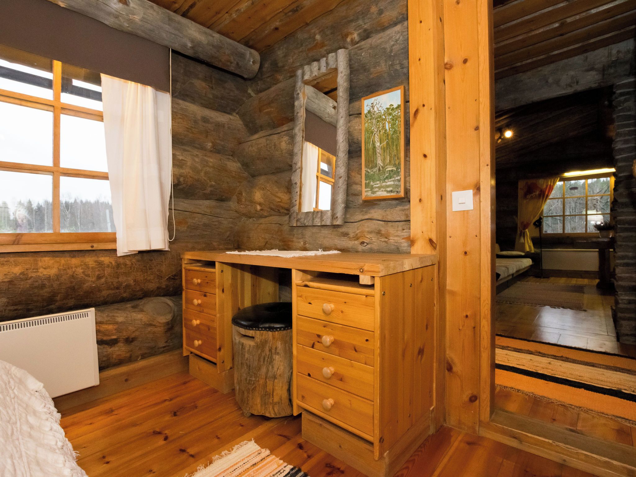 A log cabin room with a wooden dresser, a mirror, and a window with curtains.