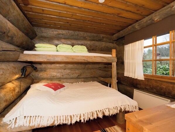 A bunk bed with a white mattress and a red pillow, a wooden table, and a window with curtains.