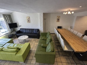 Ein modernes Wohnzimmer mit einer schwarzen Ledersofa, einem grünen Ledersofa und einem Holzesstisch mit weißen Stühlen. Ein Flachbildfernseher ist an der Wand befestigt, und über den Sofas hängen zwei gerahmte Kunstwerke.