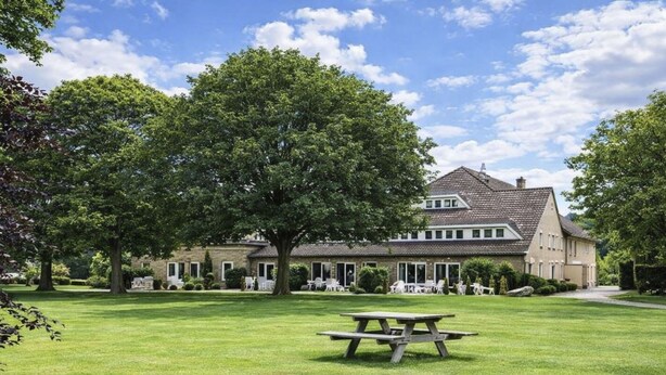 Een groot huis met een gazon en een picknicktafel op de voorgrond.