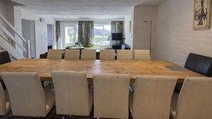 Een ruime eethoek met een lange houten tafel en zes stoelen, een televisie, en een trap naar een andere kamer.