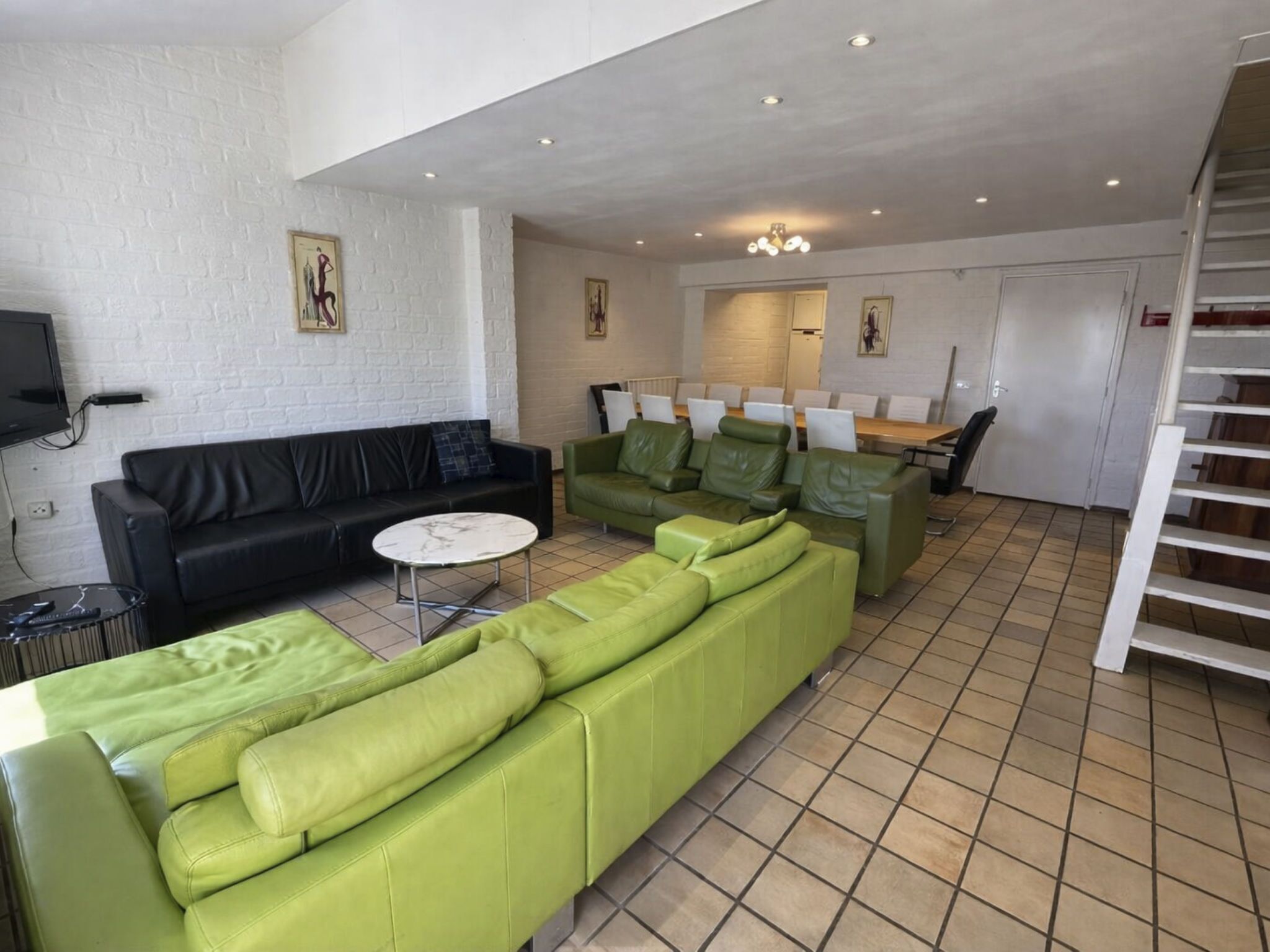 A modern living room with a black leather sofa, green leather sofas, a white coffee table, and a dining area with a wooden table and chairs.