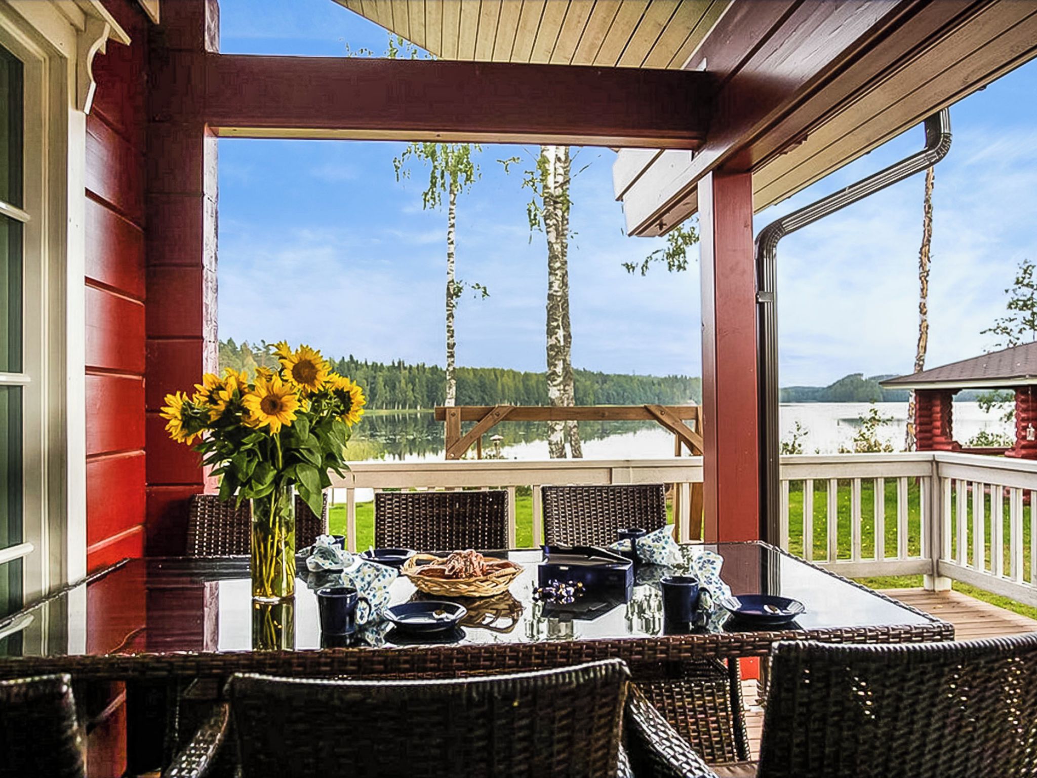 Un espace extérieur abrité, aménagé avec des tables pour prendre les repas, et offrant une vue sur un lac et une forêt.