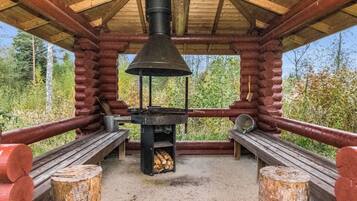 Een rustieke houten hut met een houtkachel, banken en uitzicht op het omliggende bos.