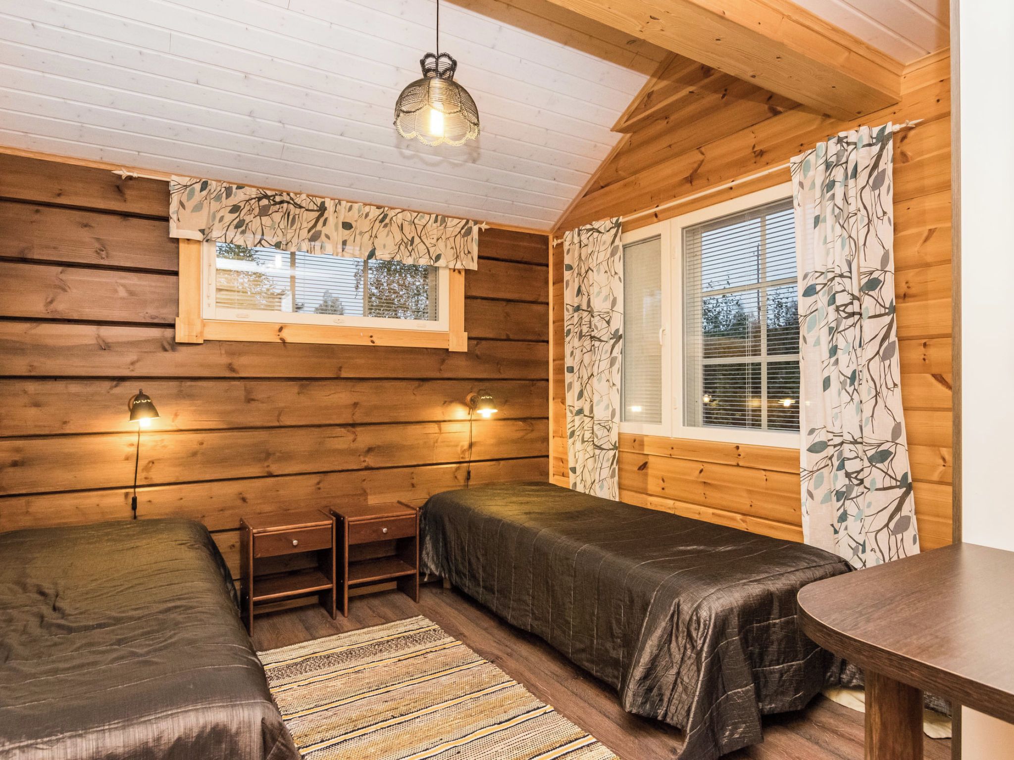 Une chambre confortable de style cabane, avec deux lits, une petite table et une fenêtre avec des rideaux.