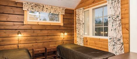 A cozy cabin room with two beds, a small table, and a window with curtains.