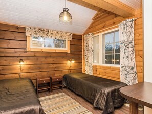 Ein gemütliches Blockhauszimmer mit zwei Betten, einem kleinen Tisch und einem Fenster mit Vorhängen.
