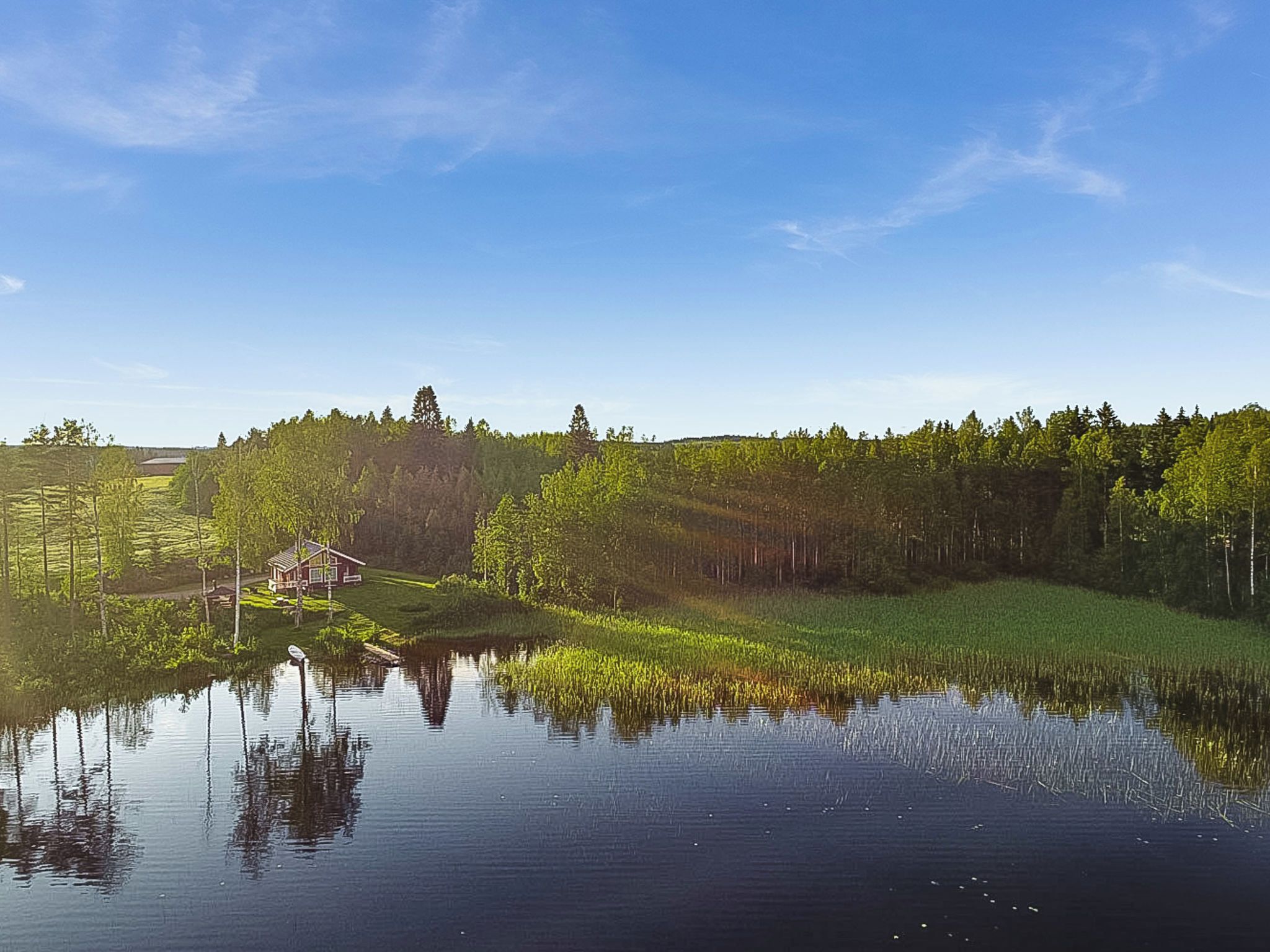 A serene lakeside scene with a house near the water's edge, surrounded by dense forest.