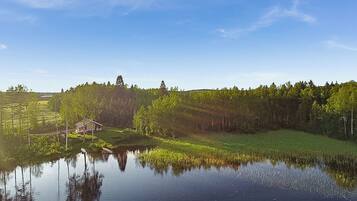 A serene lakeside scene with a house near the water's edge, surrounded by dense forest.