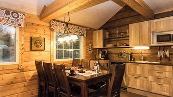 A wooden interior with a dining table set for four, kitchen cabinets, a microwave, and a hanging light fixture.