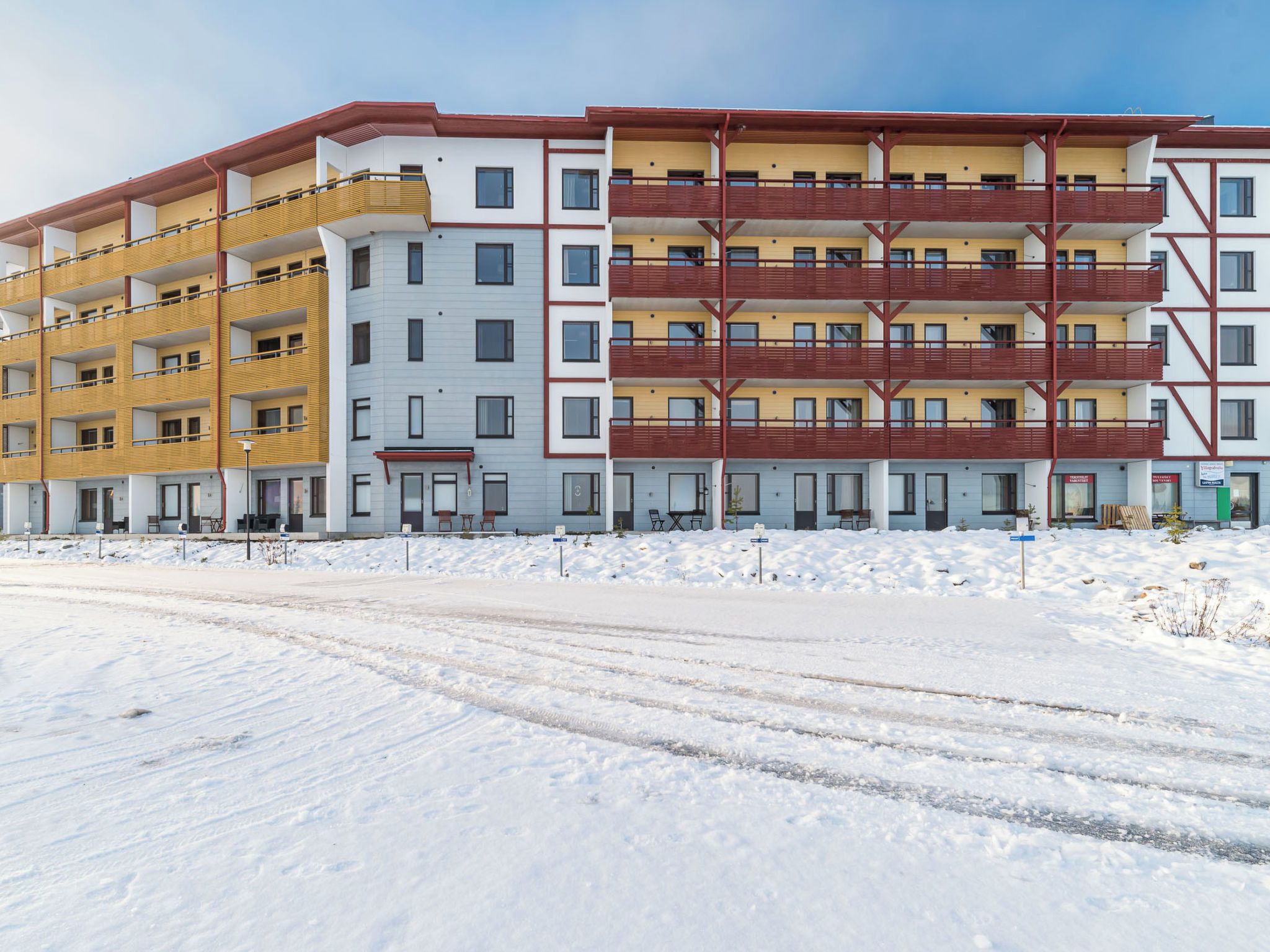 Un immeuble résidentiel à plusieurs étages, doté de balcons, d’une entrée couverte et d’un sol recouvert de neige.