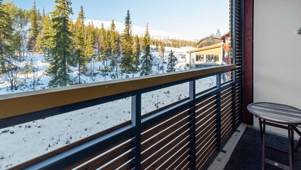 Un balcon donnant sur un paysage enneigé, un bâtiment et une chaise.
