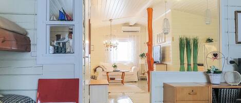A room with a red chair, a wooden cabinet with drawers, and a doorway leading to another room with a sofa and a table.