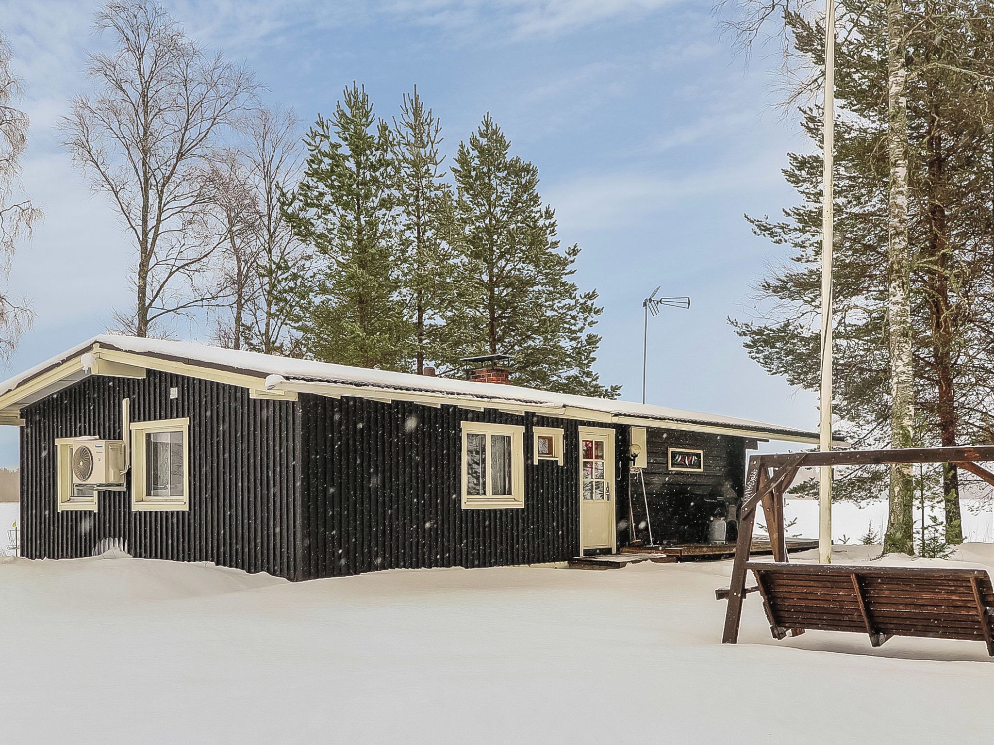 A small, single-story building with a black exterior and white trim, surrounded by snow and trees.