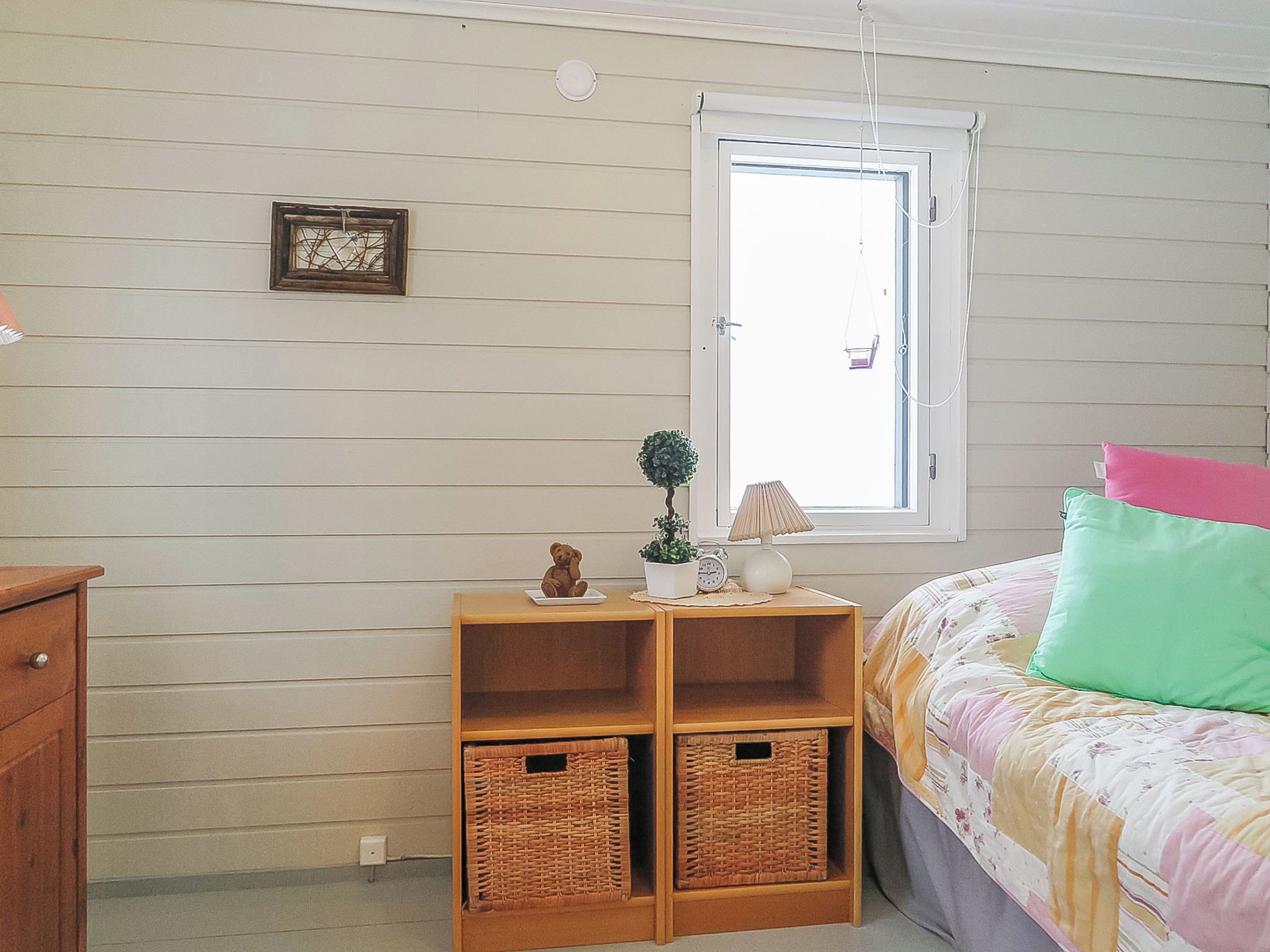 Un dormitorio con cama, una mesita de noche con lámpara, un ventanal pequeño y un cuadro colgado en la pared.
