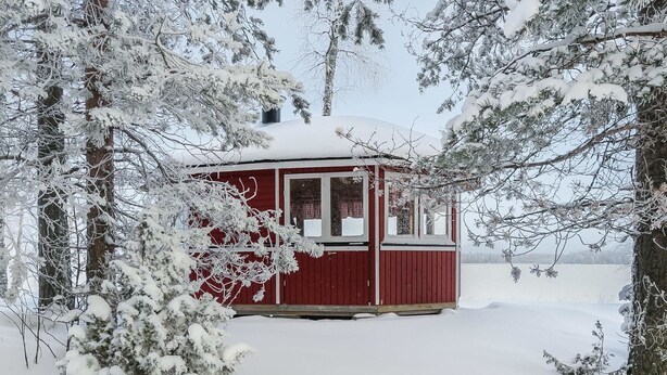 Una cabaña pequeña y roja rodeada de árboles cubiertos de nieve.
