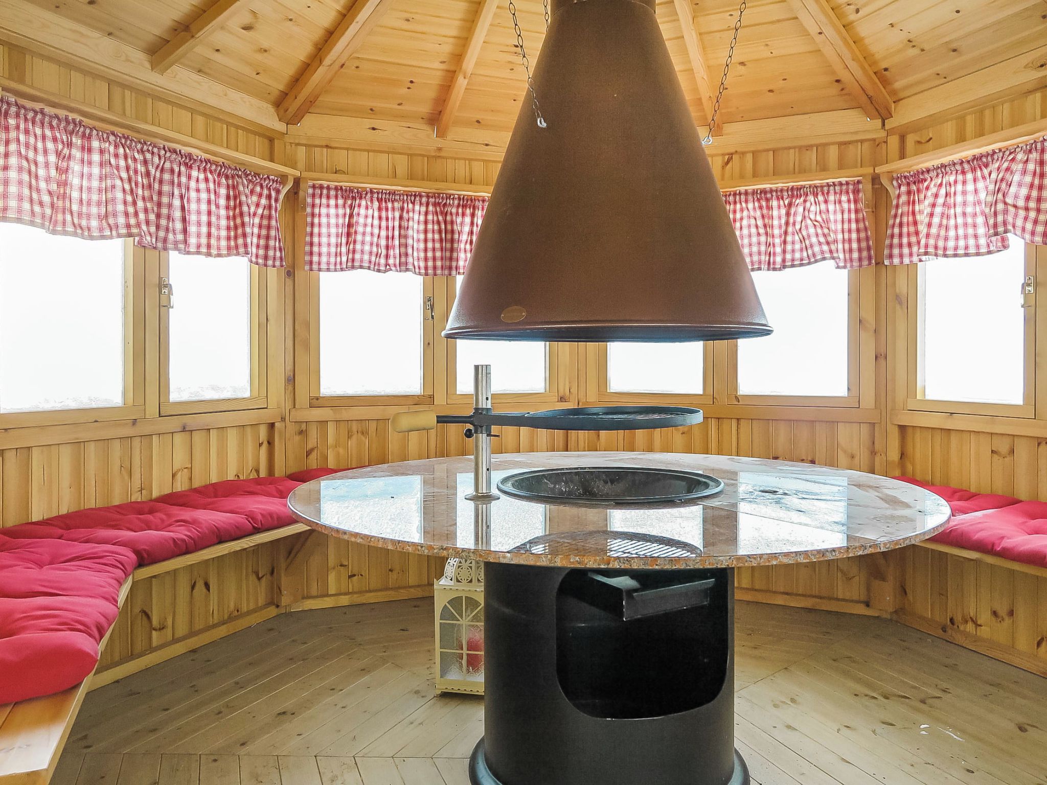 Een houten interieur met een ronde tafel, rode zachte zitplaatsen en een grote hanglamp.