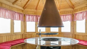 Una cabaña de madera con una mesa redonda, bancos tapizados en rojo y una lámpara colgante grande.