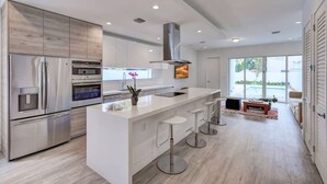A modern kitchen with stainless steel appliances, a white island with bar stools, and a view of a swimming pool. -  Poolside Sanctuary 4B 4B heated pool ,Jacuzzi 1Gb internet.  (Miami)