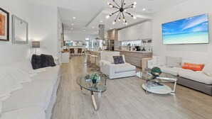 A modern living room with a glass coffee table, white sofas, and a large TV screen displaying a beach scene. -  Poolside Sanctuary 4B 4B heated pool ,Jacuzzi 1Gb internet.  (Miami)