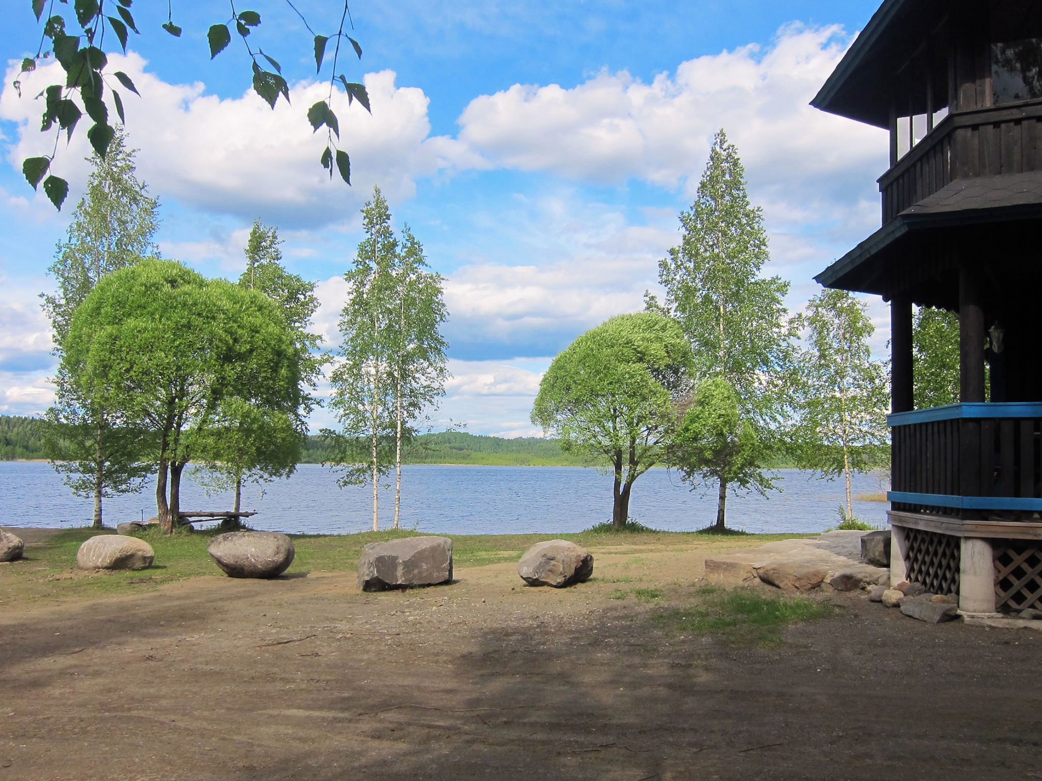 Näkymä järvelle, jossa on puinen mökki, suuria kiviä ja puita.