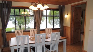 A dining area with a wooden table and white chairs, large windows with curtains, and a wooden ceiling. - Kiviniemi by Interhome (Tohmajärvi)