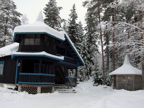 A snow-covered lodge with a prominent chimney, surrounded by tall evergreen trees. - Kiviniemi by Interhome (Tohmajärvi)