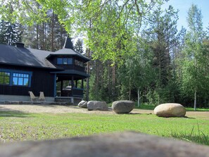 A wooden cabin with a dark roof, surrounded by a grassy area and large rocks. - Kiviniemi by Interhome (Tohmajärvi)