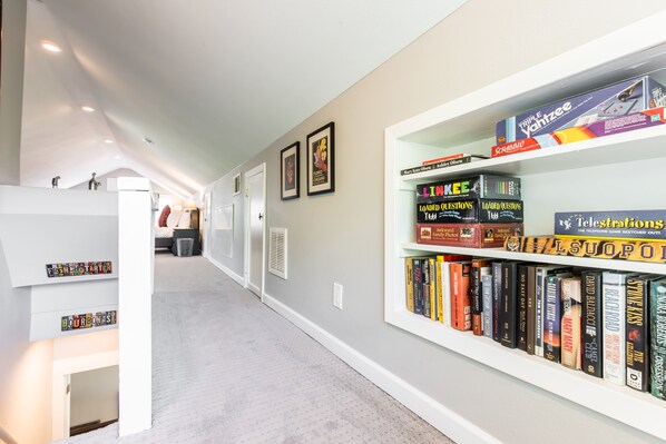 A hallway with a bookshelf containing various board games and books. - The Roux House Offers Luxury, Comfort & Location! (Dallas)