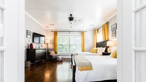 A bedroom with a bed, bedside tables, a desk, a chair, a TV, and a window with curtains.