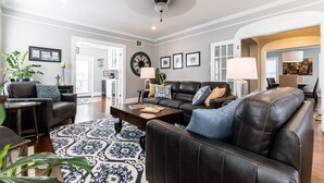 A spacious living room with a large black leather sofa, a patterned rug, and a ceiling fan.