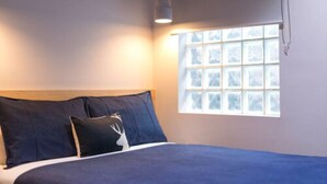 Une chambre à coucher avec un lit, deux oreillers, une fenêtre et un luminaire suspendu.