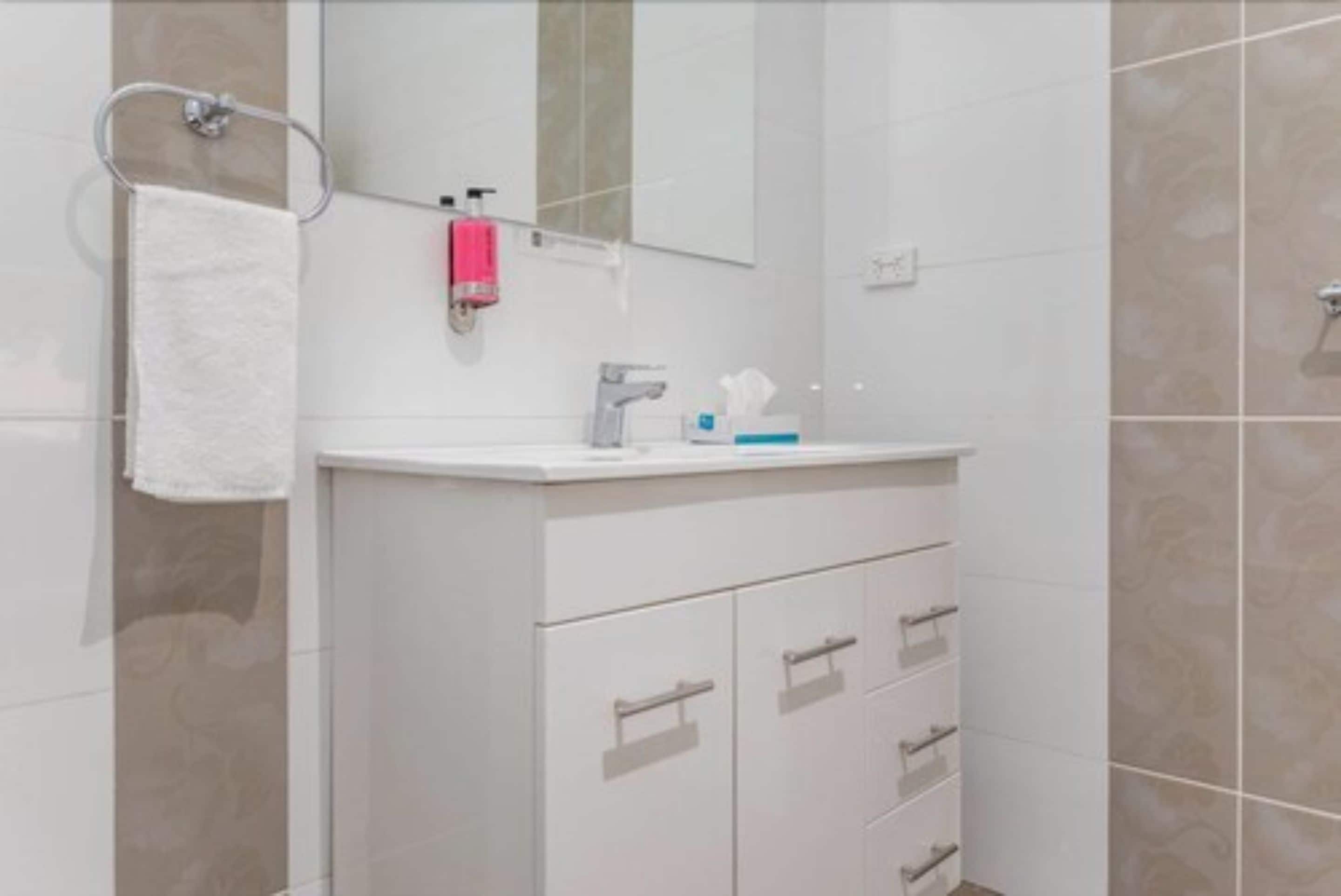 A modern bathroom with a white vanity, a towel rack, a mirror, and a soap dispenser.