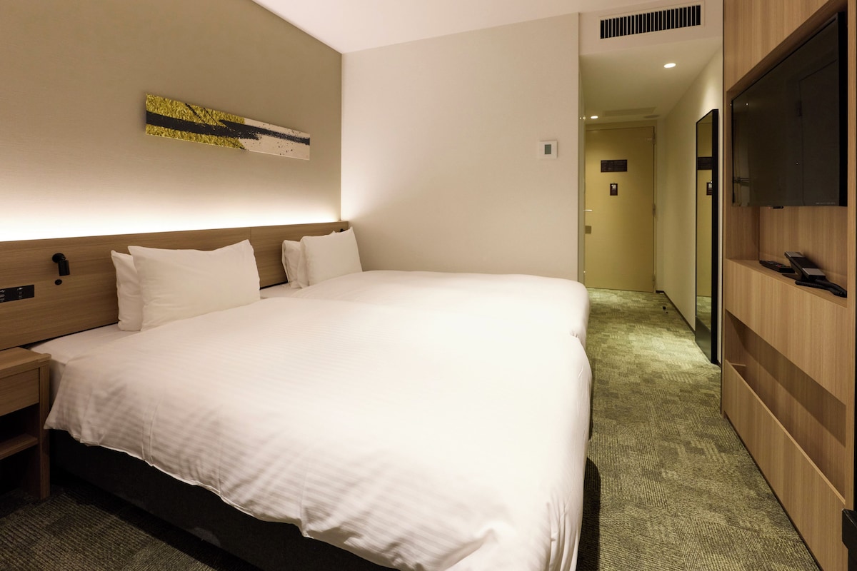 Una habitación de hotel moderna con una cama grande, un televisor de pantalla plana, cabecero de madera y piso alfombrado.