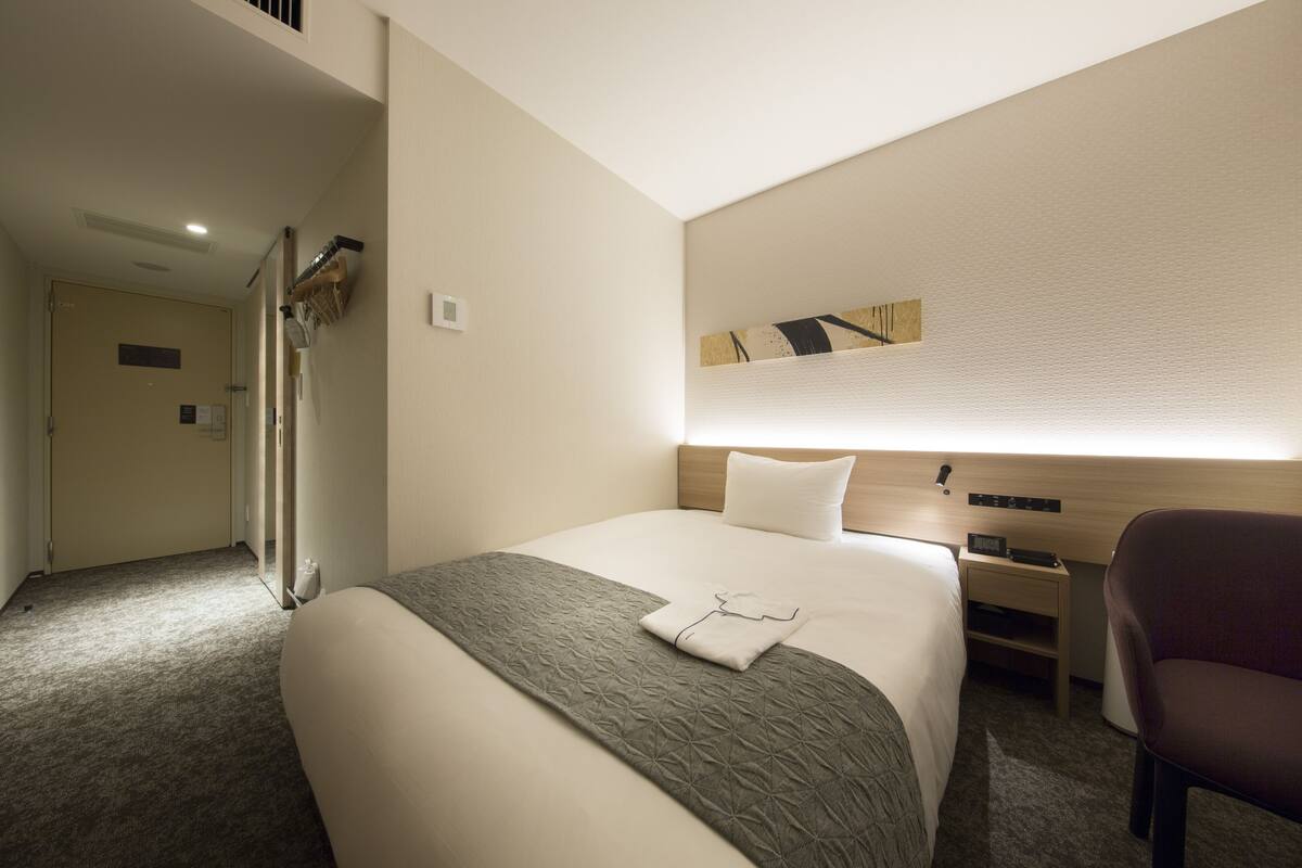 A hotel room with a neatly made bed, a desk with a chair, and a mirror.