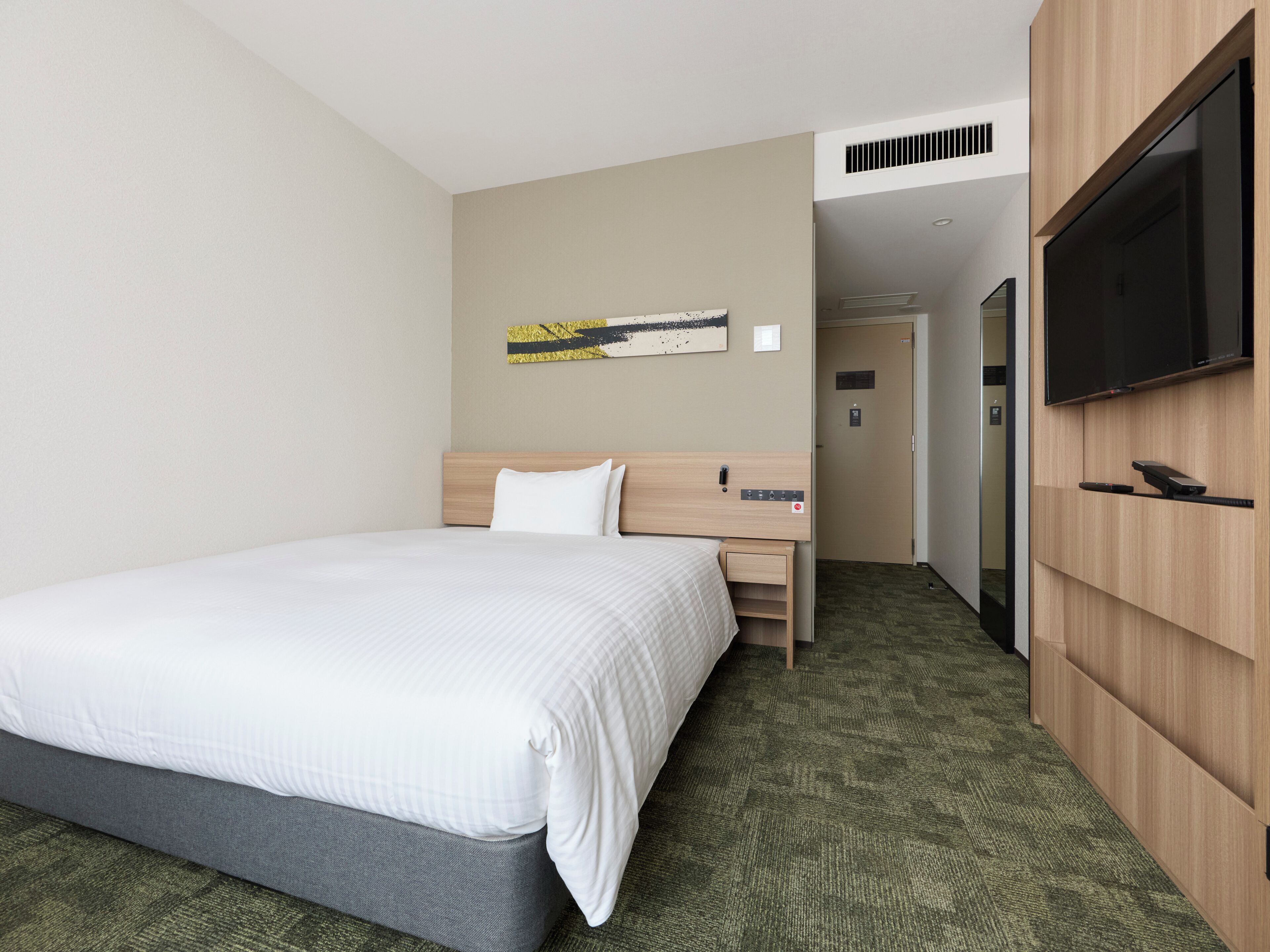 A hotel room with a bed, a desk, a television, and a wall-mounted artwork.