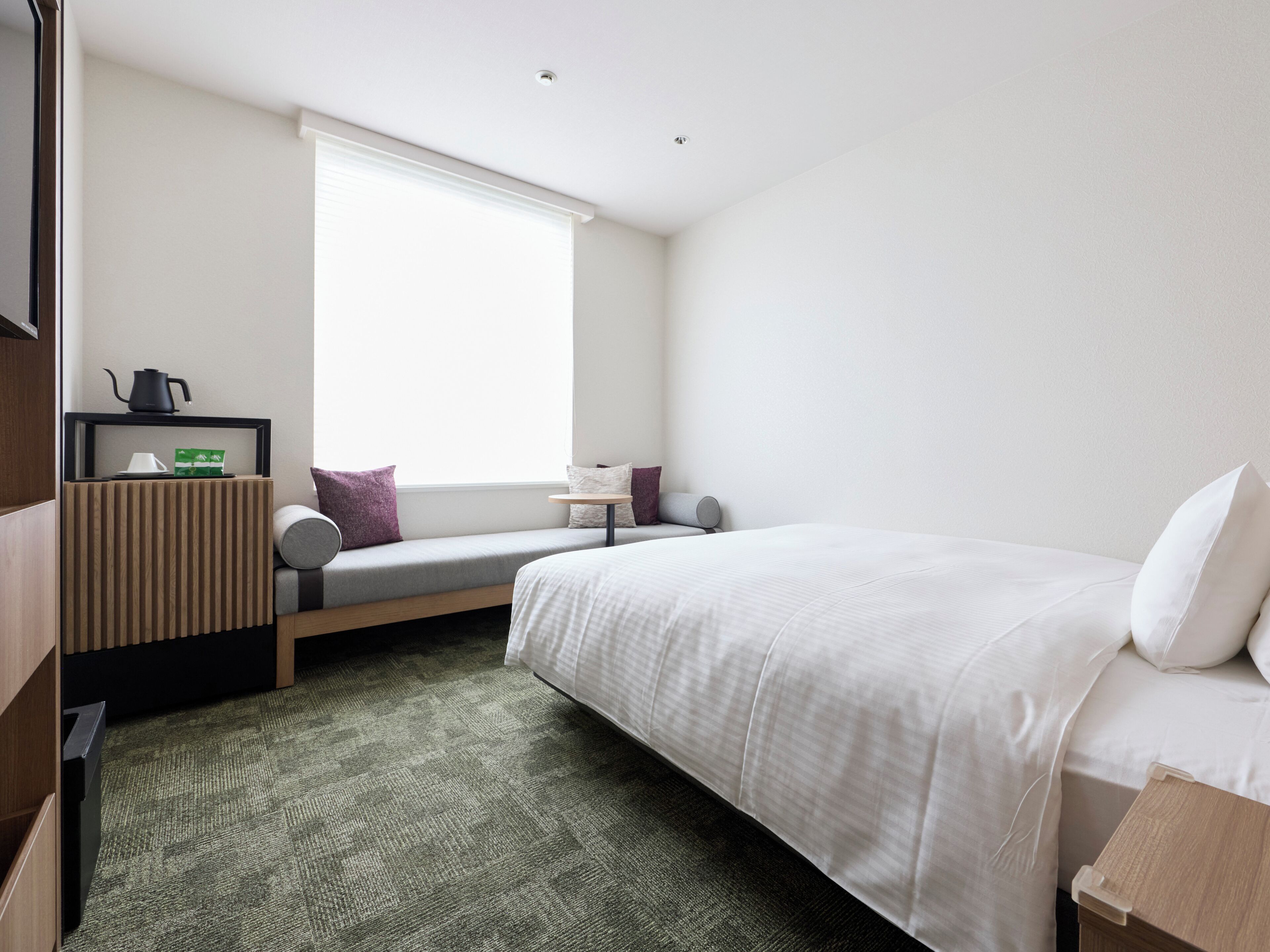 Une chambre d’hôtel avec un lit, une petite table, un banc et une fenêtre.