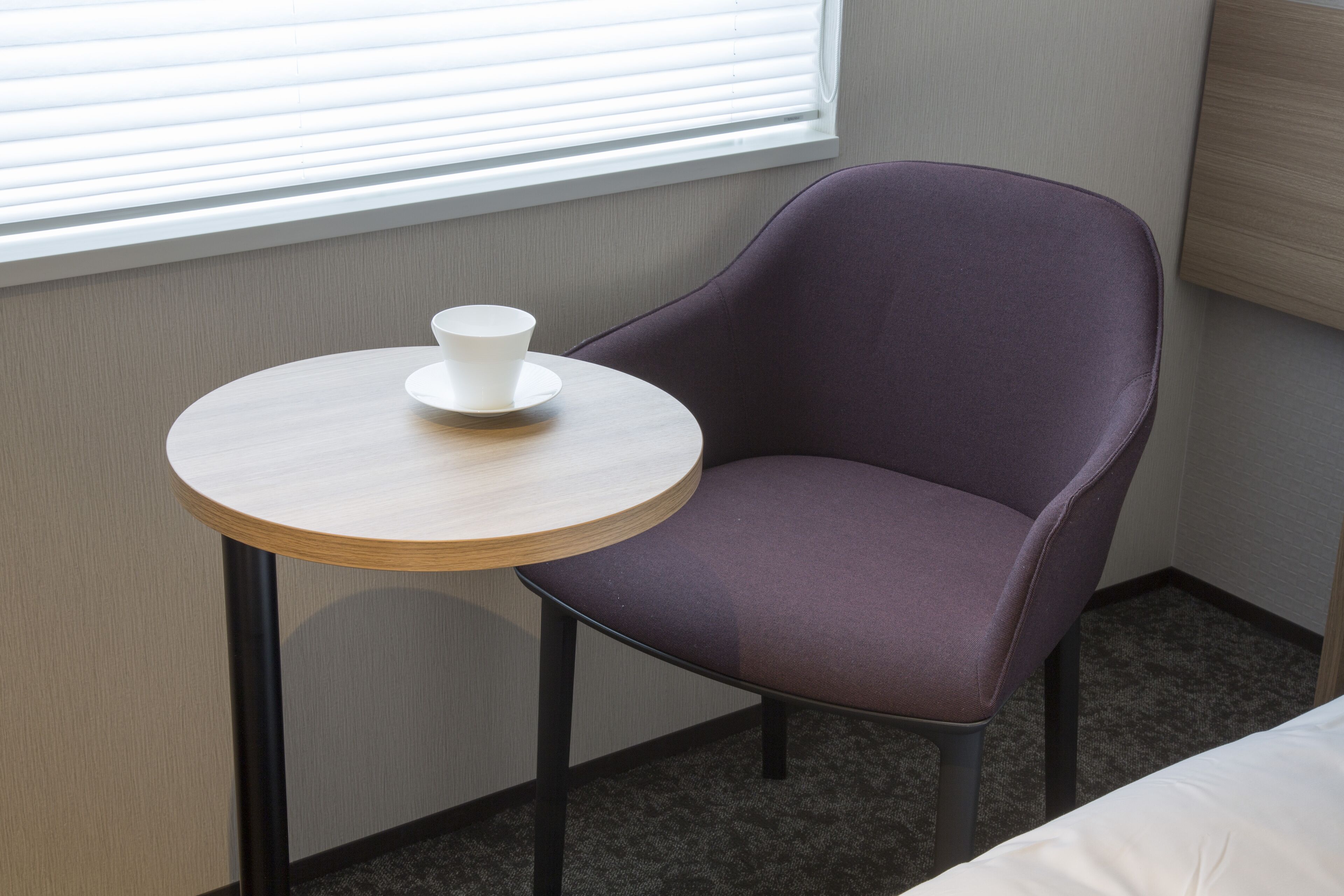 A room with a round table, a purple chair, a white cup, and a window with blinds.