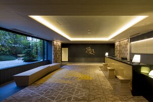 A modern reception area with a geometric patterned floor, a reception desk, and a view of a garden through large windows.