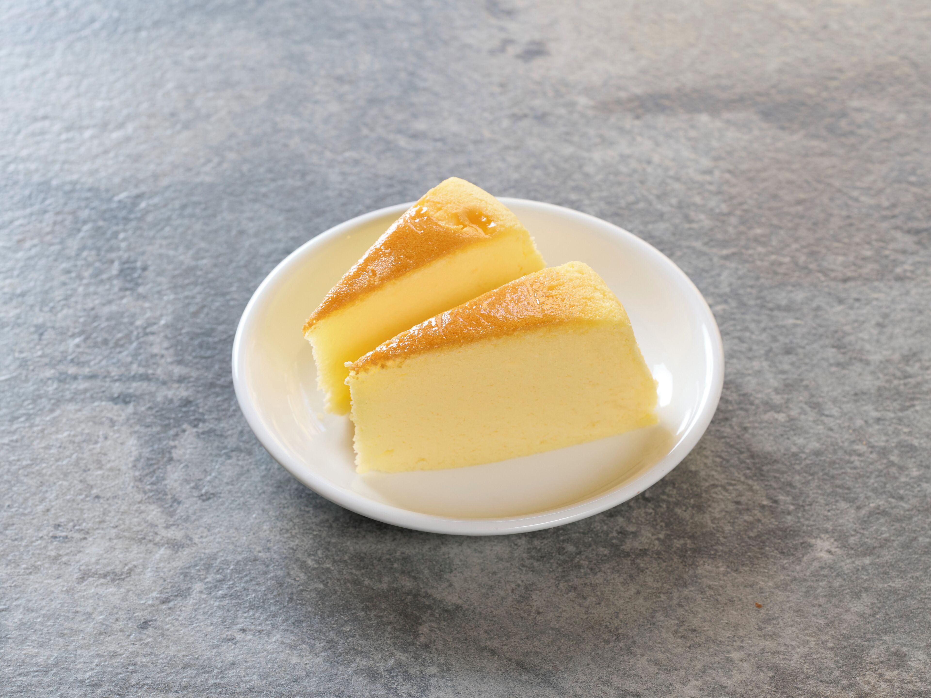 A white plate with two slices of yellow cake on a textured gray surface.