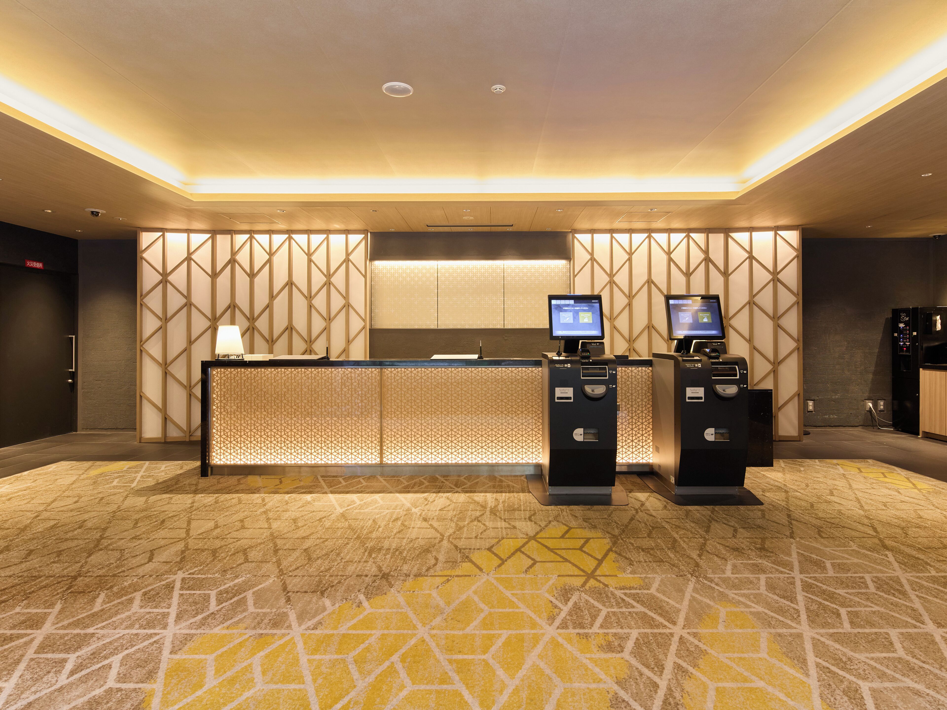 A reception area with a counter, two self-service kiosks, and a patterned wall.