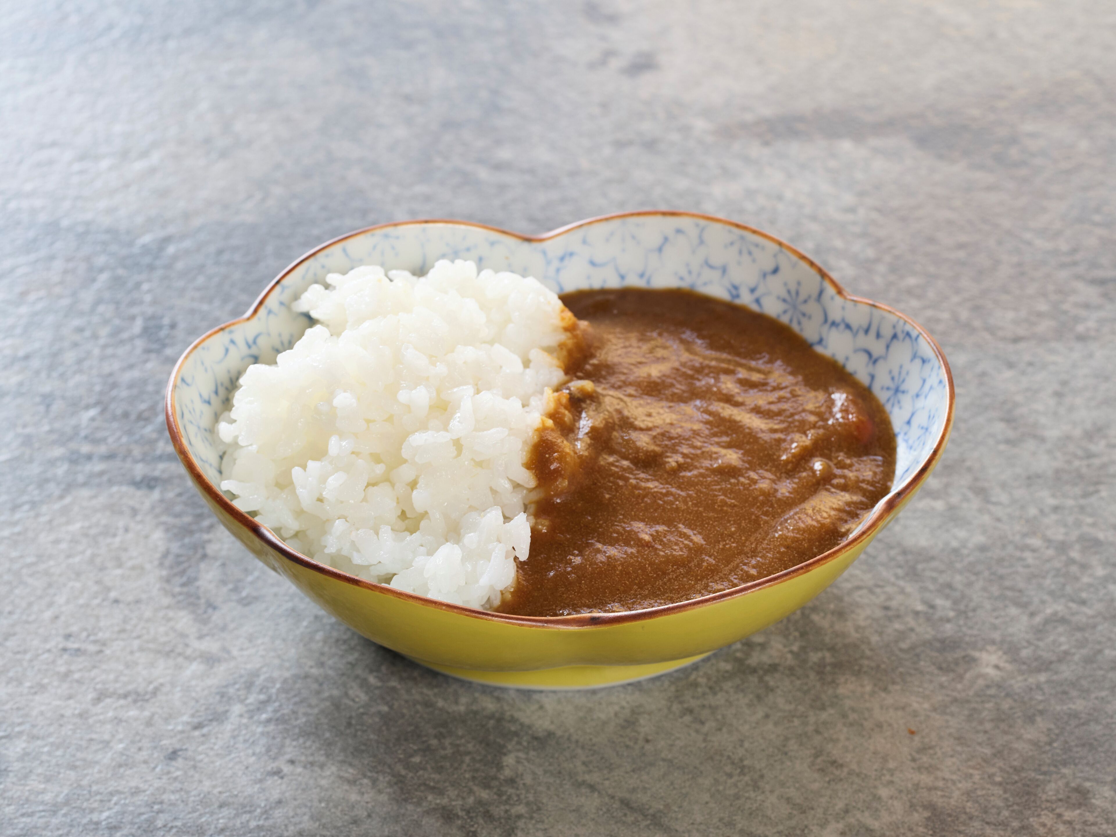 A bowl of white rice and brown sauce on a textured surface.