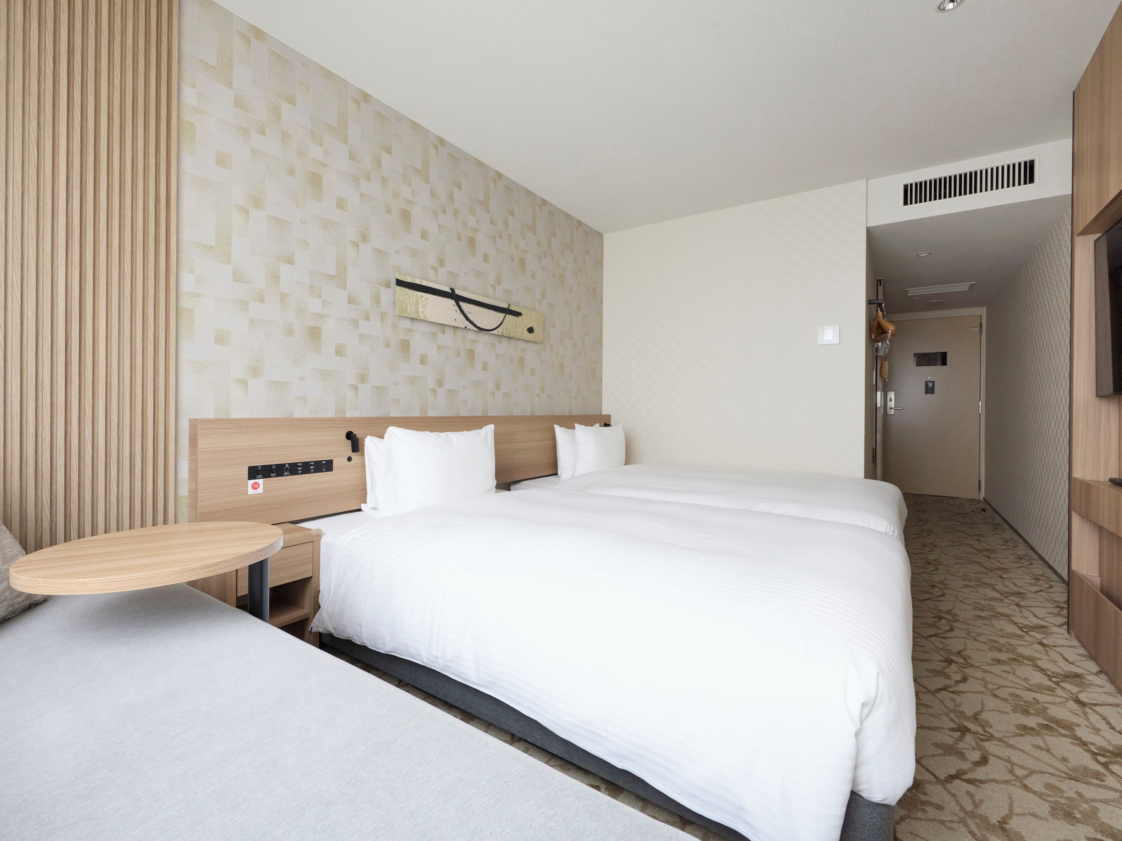 Habitación de hotel con una cama grande, una mesita de noche, un panel de control en la pared y una alfombra estampada.