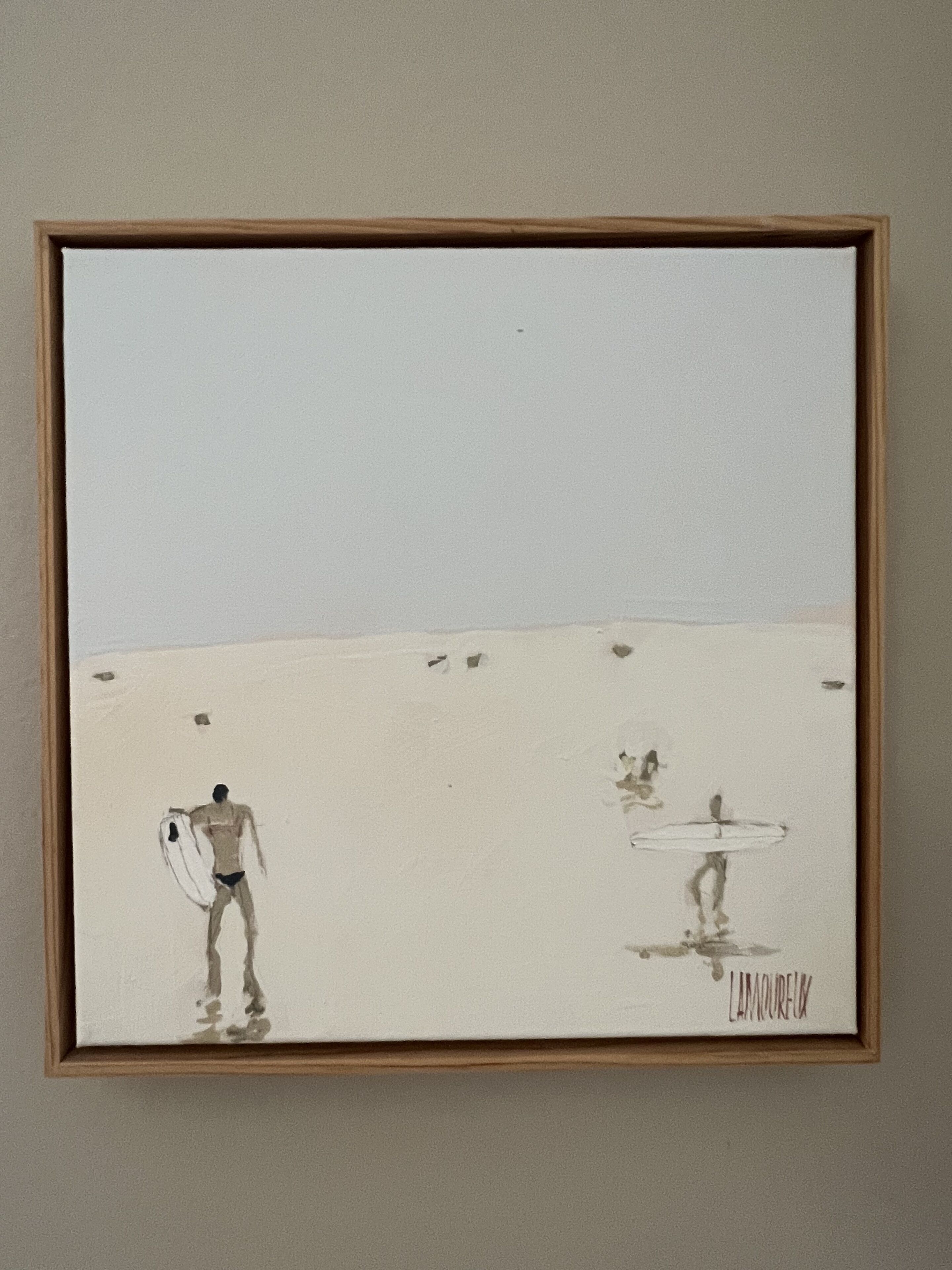 Una obra d'art emmarcada que representa dues figures a la platja, una d'elles carregant una taula de surf.