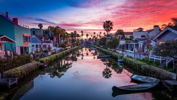 Un canal flanqueado por casas y barcos, reflejando el cielo al atardecer.