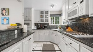 Una cocina moderna con armarios blancos, encimeras de granito y estufa empotrada.