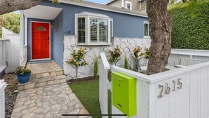 Una casa con puerta roja, sendero de piedra, pequeño jardín y valla blanca con el número 2815.