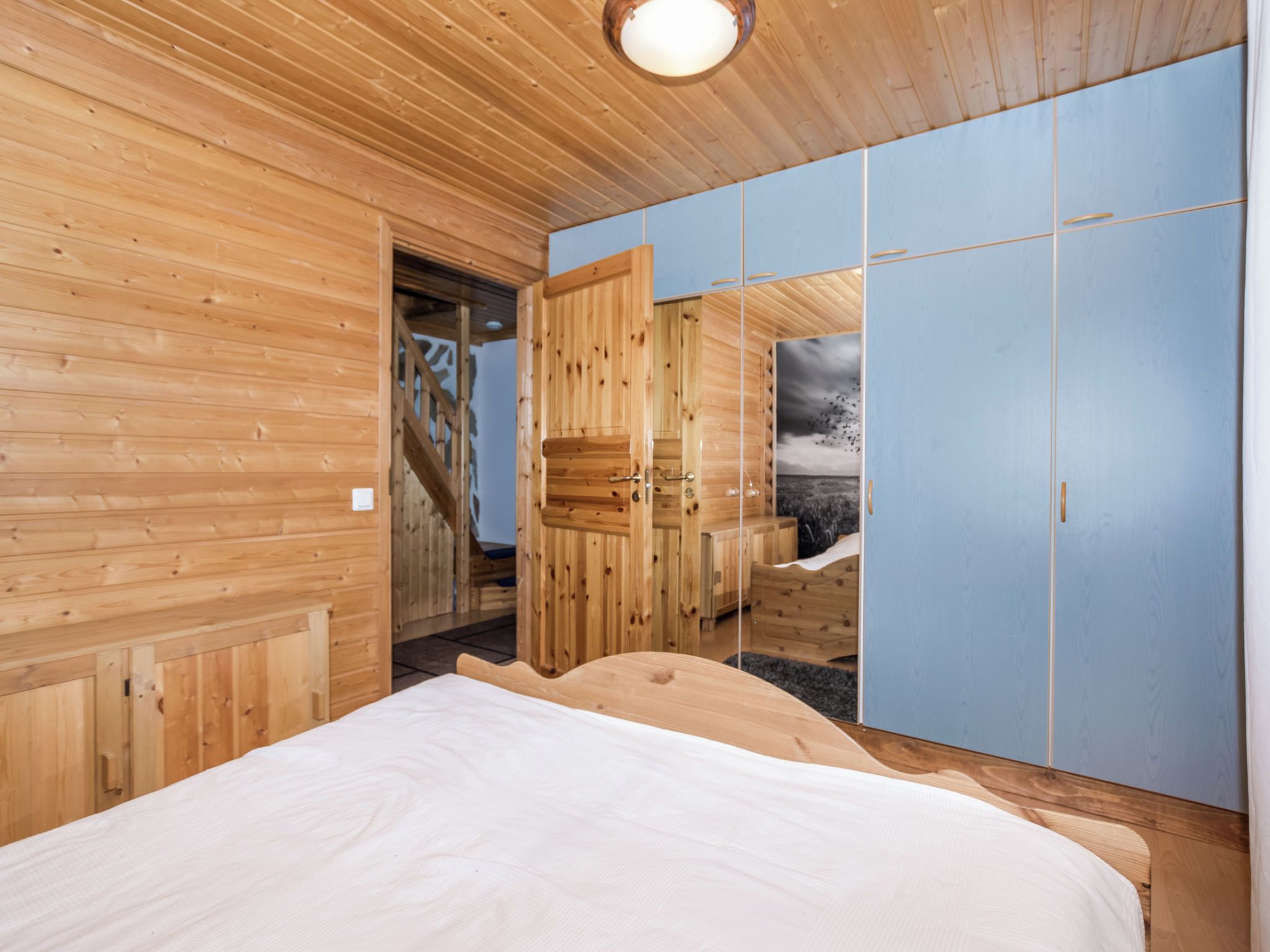 Een kamer met houten vloeren, een bed, een kledingkast en een deur die naar een trap leidt.