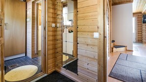 A wooden cabin interior with a shower area, a small kitchen, and a seating area.