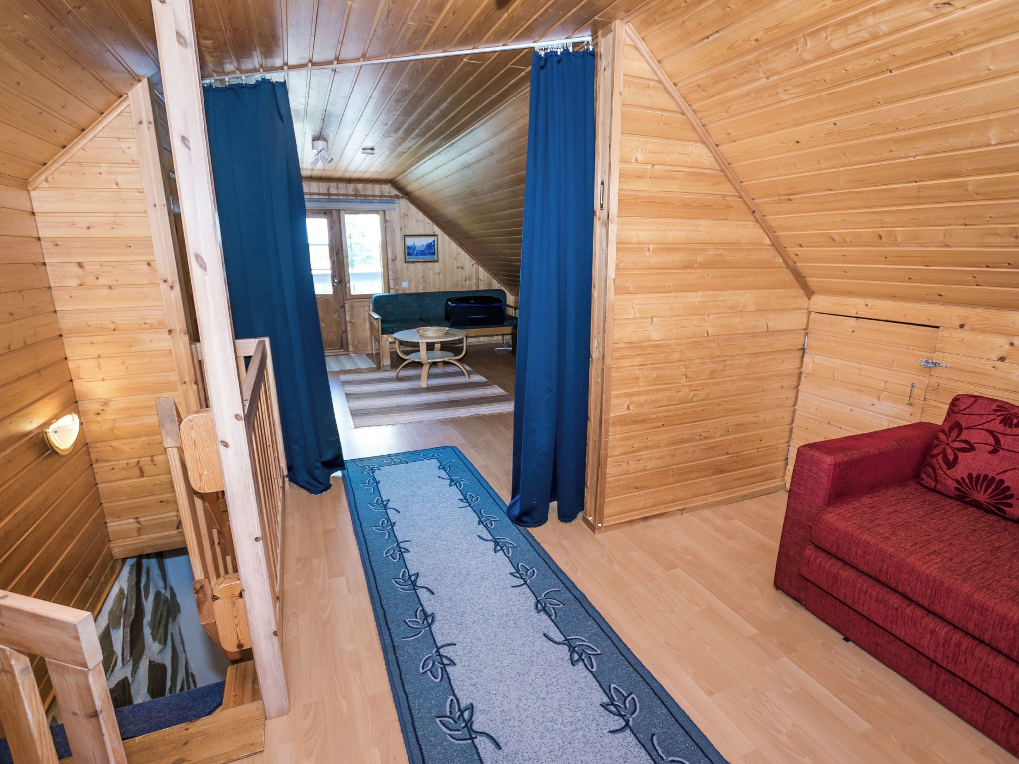 Een houten cabin met een bank, een rode stoel, een blauw gordijn en een houten trap.